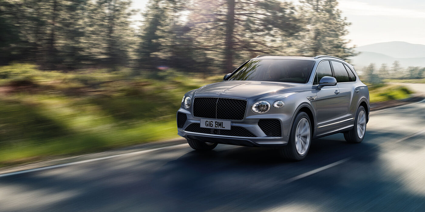 Bentley Hong Kong - DCH Bentley Bentayga luxury SUV front three quarter in Moonbeam paint, driving on an country road past trees.