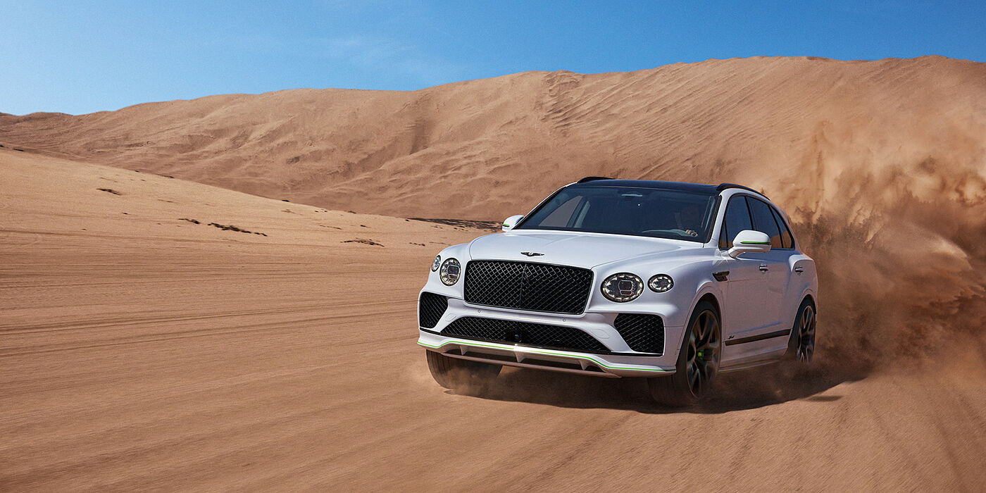 Bentley Hong Kong - DCH Bentley Bentayga Speed SUV front three quarter in Snow Quarts Pearlescent by Mulliner white paint driving dynamically through the desert