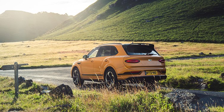 Bentley Hong Kong - DCH Bentley Bentayga S SUV rear three quarter in Sunburst Gold paint on a road surrounded by green hills