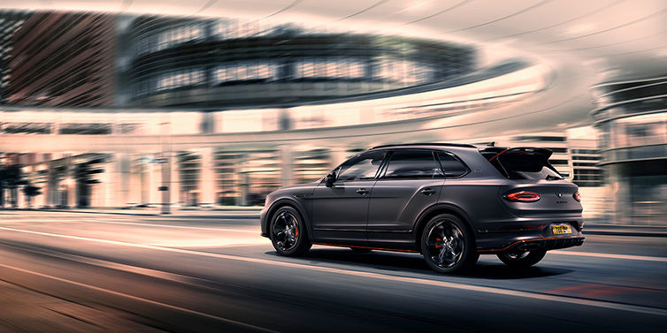 Bentley Hong Kong - DCH Bentley Bentayga S Black Edition SUV rear three quarter in Anthracite Satin paint driving dynamically through a city at night