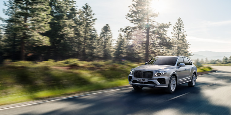 Bentley Hong Kong - DCH Bentley Bentayga SUV front three quarter in Moonbeam silver paint driving dynamically along a tree-lined road