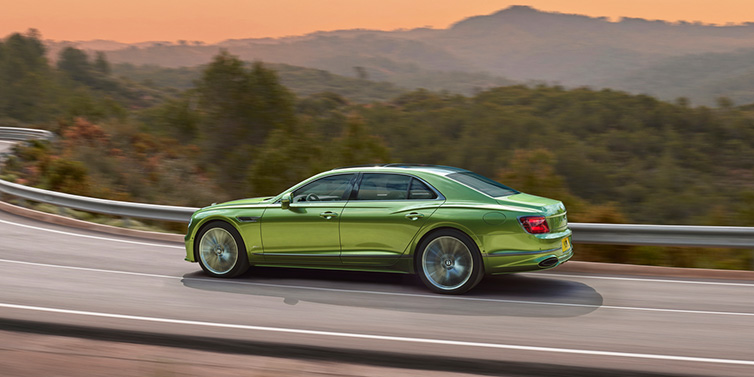 Bentley Hong Kong - DCH Bentley Flying Spur Speed sedan side profile in Tourmaline Green paint driving dynamically on a mountain road at sunset