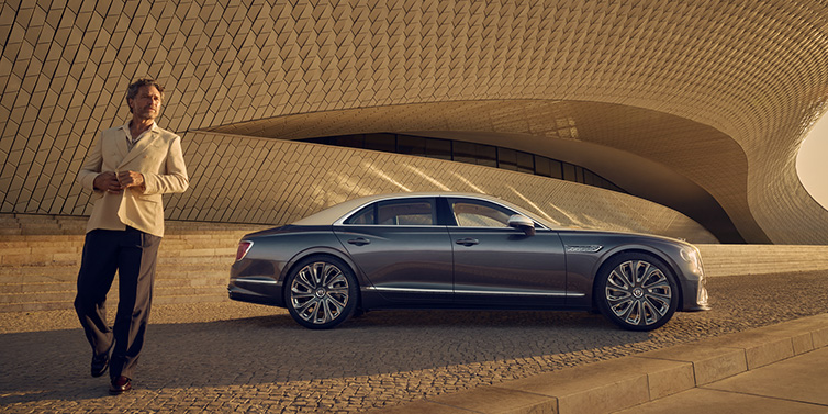 Bentley Hong Kong - DCH Bentley Flying Spur Mulliner sedan in Rose Gold over Magnetic duotone paint parked by a curved wall with person in suit jacket standing on the left